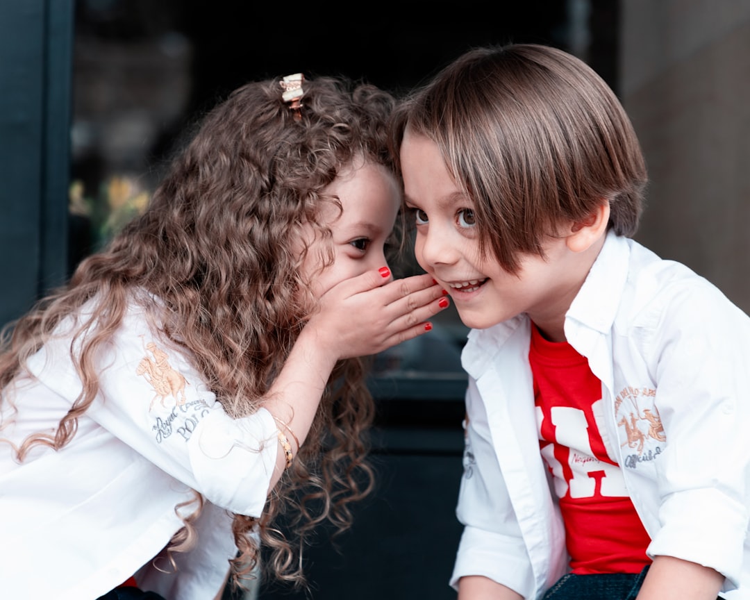 A girl with long curly hair whispering into the ear of a boy